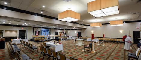 Une grande salle de conférence avec des rangées de chaises, des tables et une estrade.