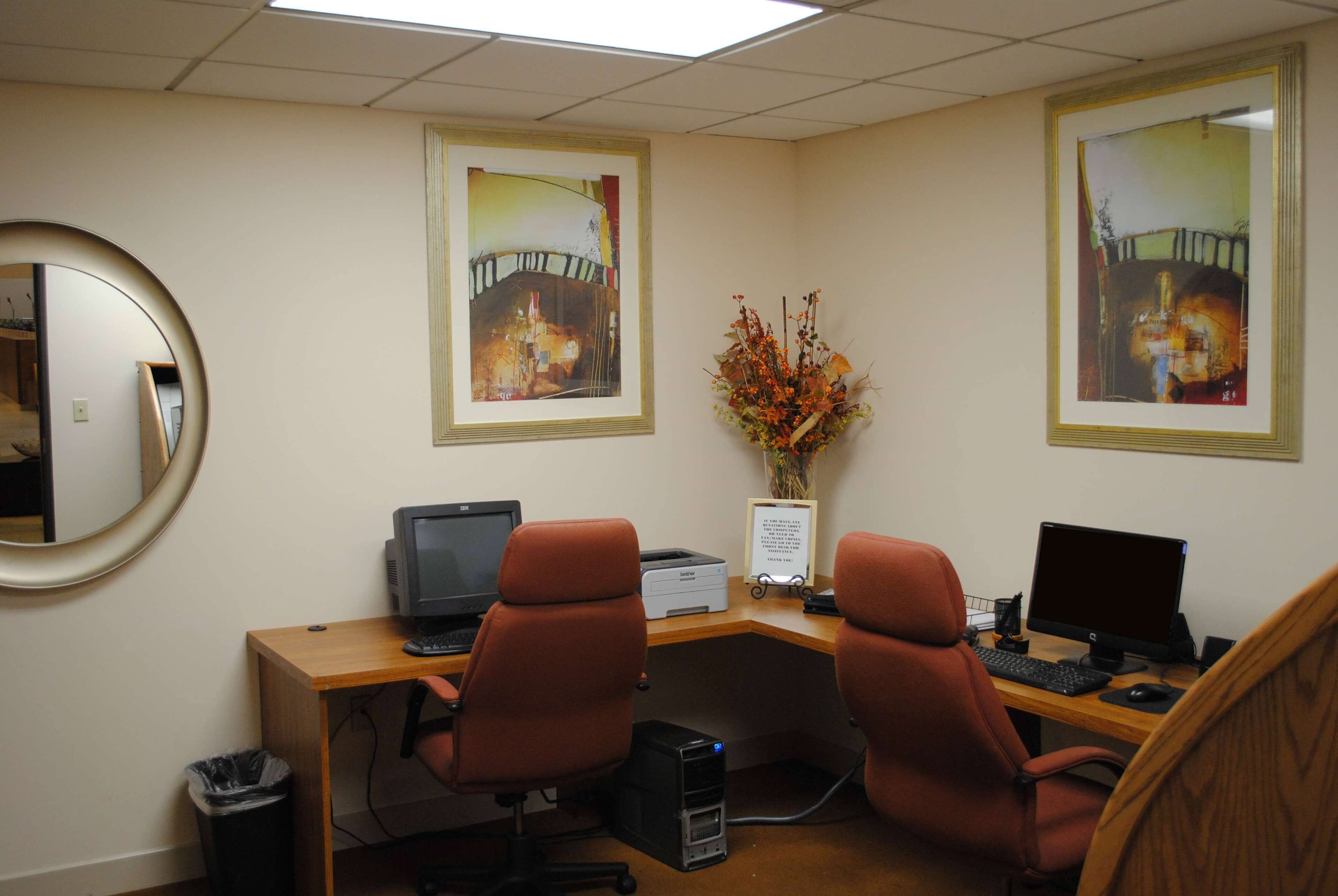 An office with two desks, each with a computer and chair. There is a mirror on the left, and two framed pictures on the wall.