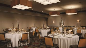 Una sala de banquets amb taules rodones preparades per dinar, amb teles de taula blanques i elements decoratius al centre.