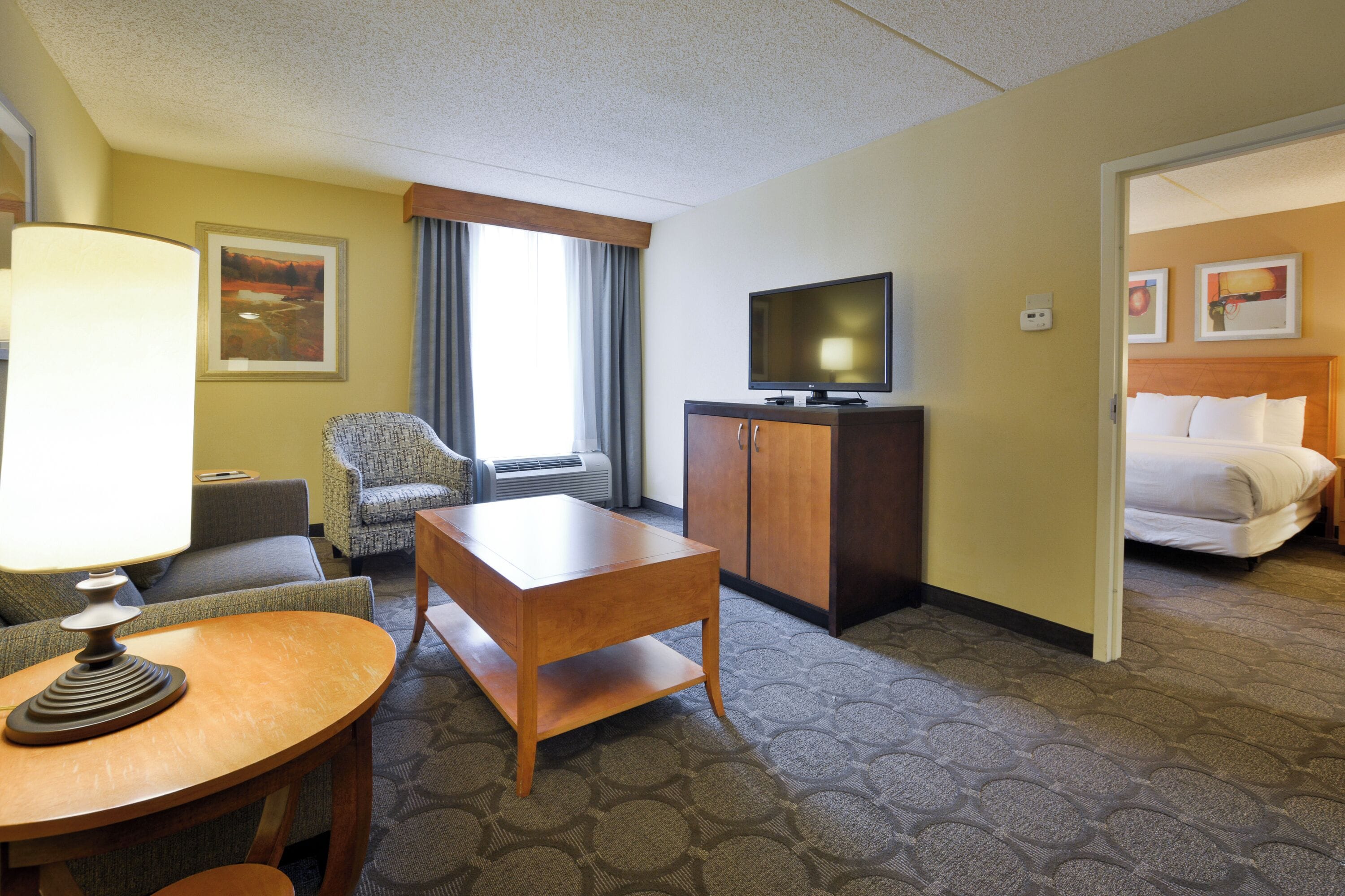 A hotel room with a bed, a television, a desk, a chair, and a lamp.