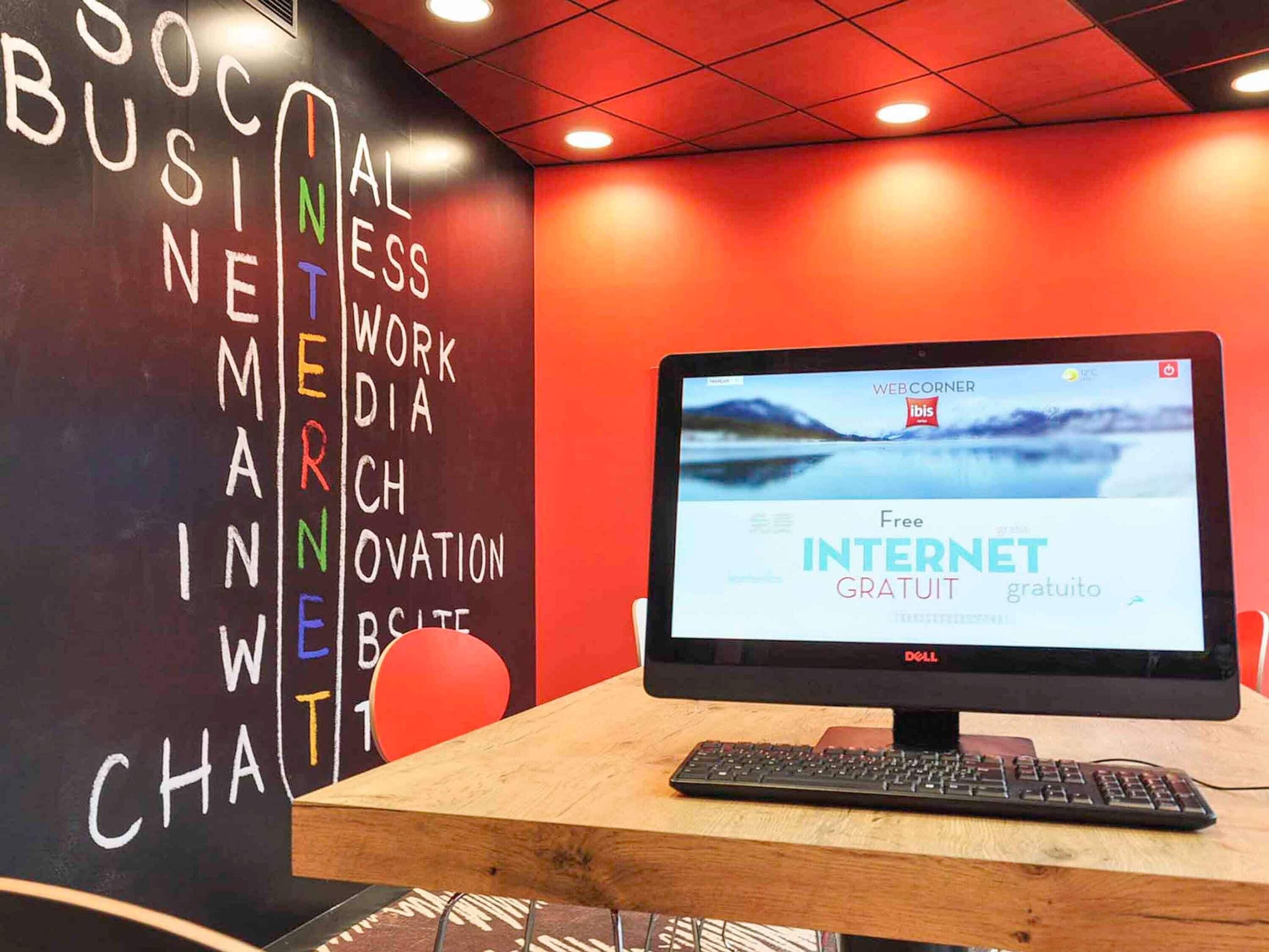 Una computadora con una pantalla que muestra 'Free INTERNET GRATUITO' en varios idiomas, una pizarra con palabras coloridas y una pared roja.