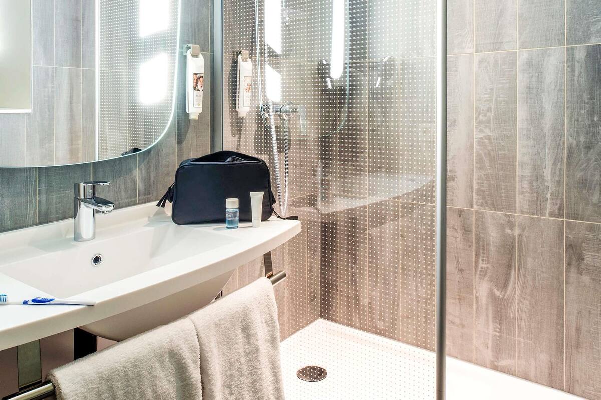 A modern bathroom with a large mirror, a sink, and a shower area.