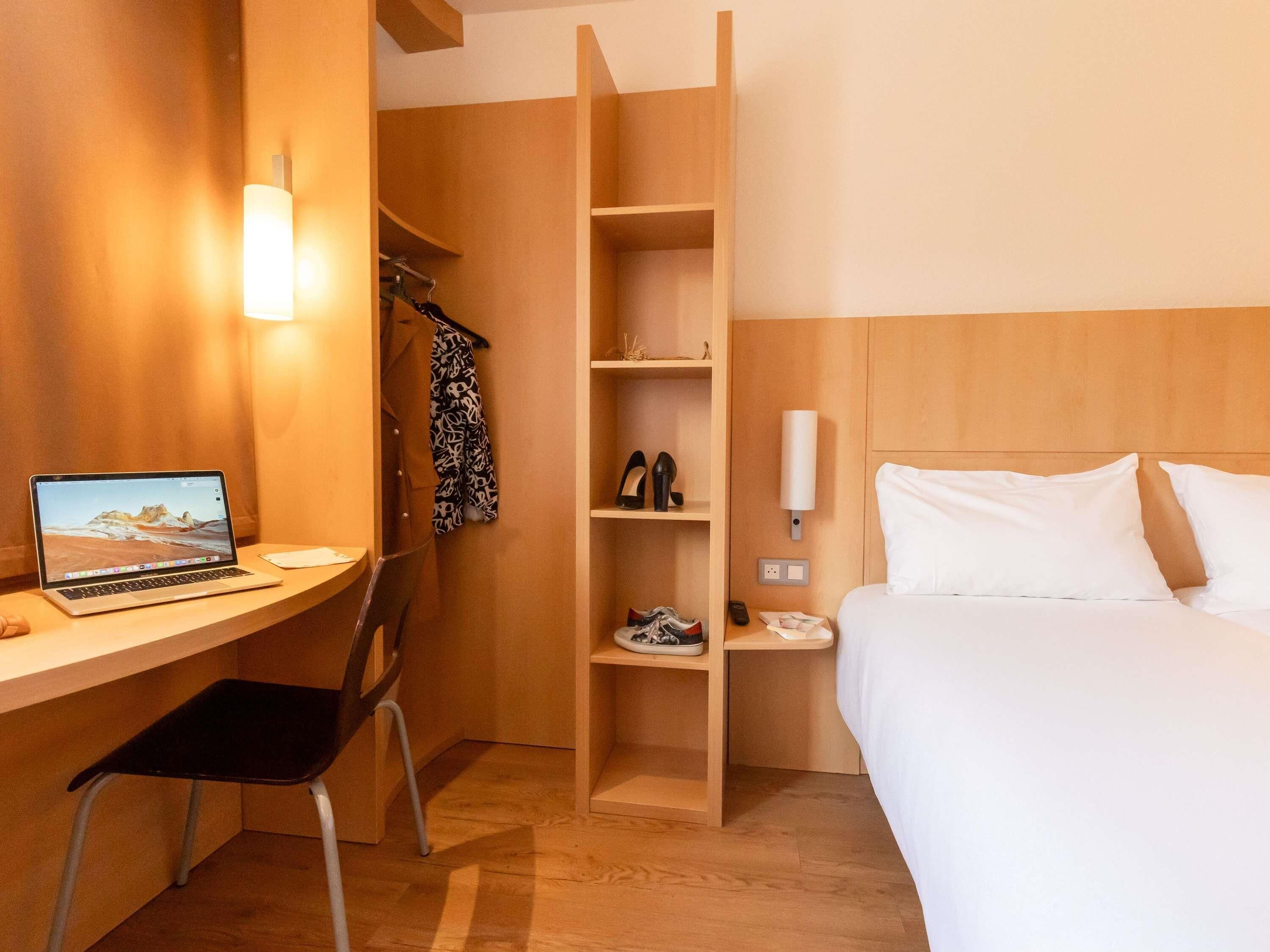 Een hotelkamer met een bureau, laptop, stoel, bed en ingebouwde planken.