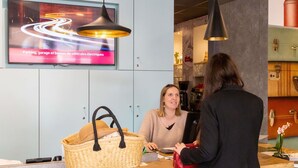 A reception desk with a large woven basket and a red handbag on it. There is a television mounted on the wall displaying a message in French about parking and garages for electric vehicles.