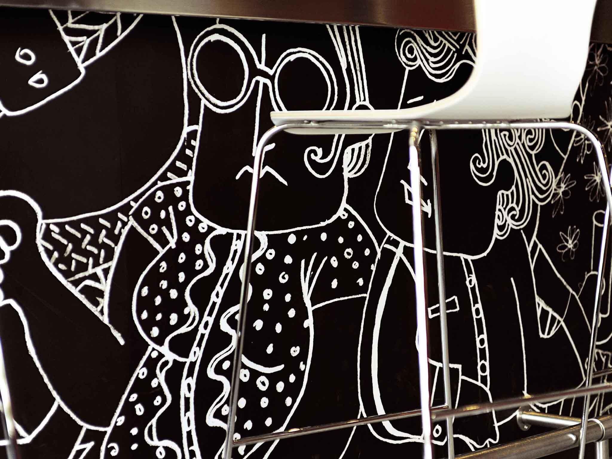 A close-up of a black and white line drawing on a surface, with a metal structure partially visible in the foreground.