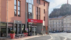 A hotel with a red sign, outdoor seating, and a view of a mountain.