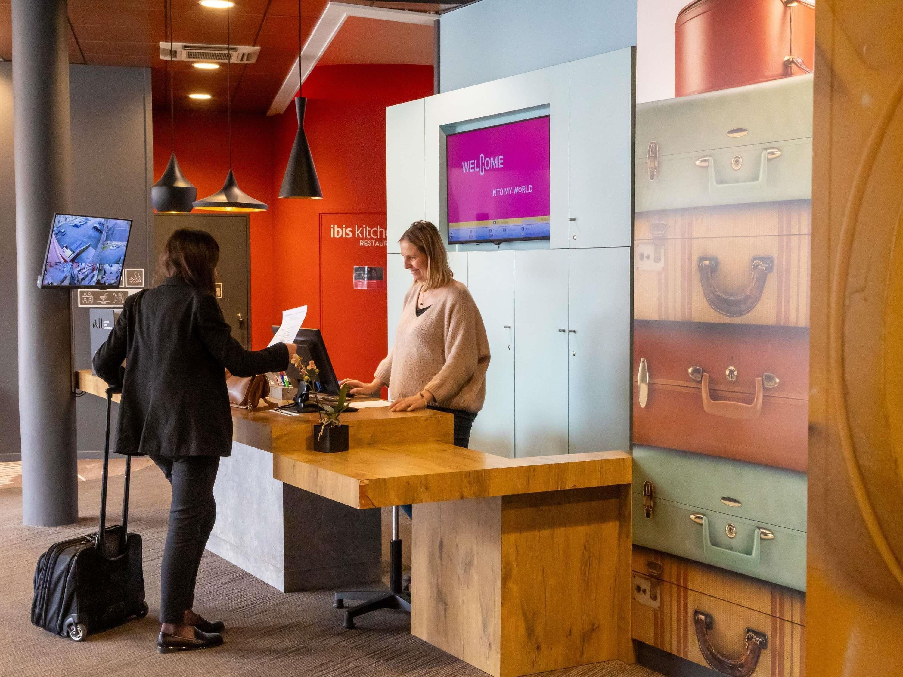 A reception desk with a digital screen displaying "WELCOME INTO MY WORLD" and a "KITCHEN" sign in the background.