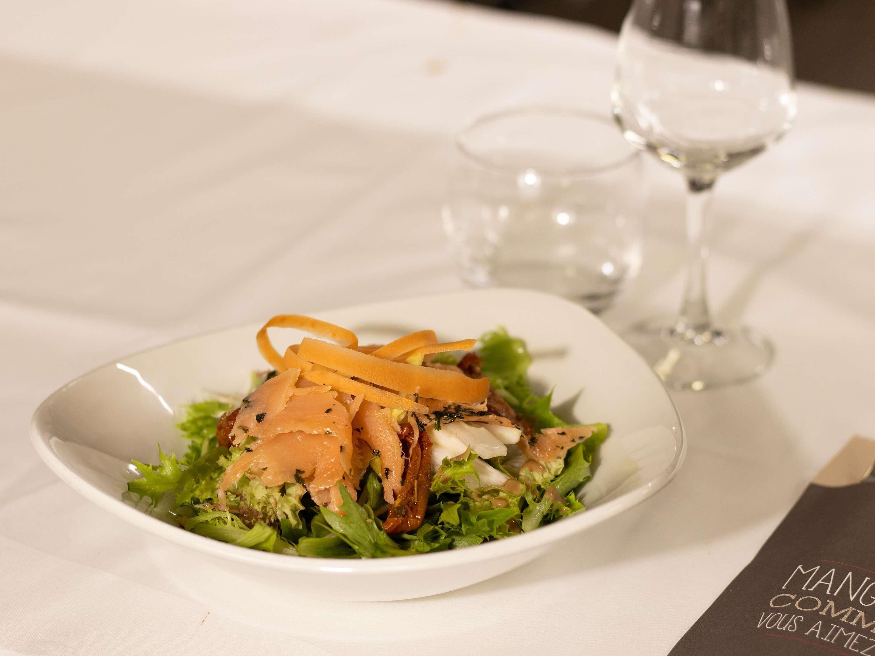 Ein weißer Teller mit Salat, ein Glas Wasser und ein Weinglas auf einem Tisch.