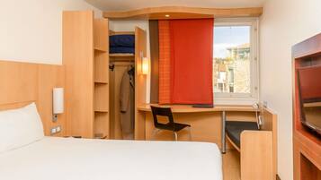 A hotel room with a bed, a desk, a chair, a wardrobe, and a TV.