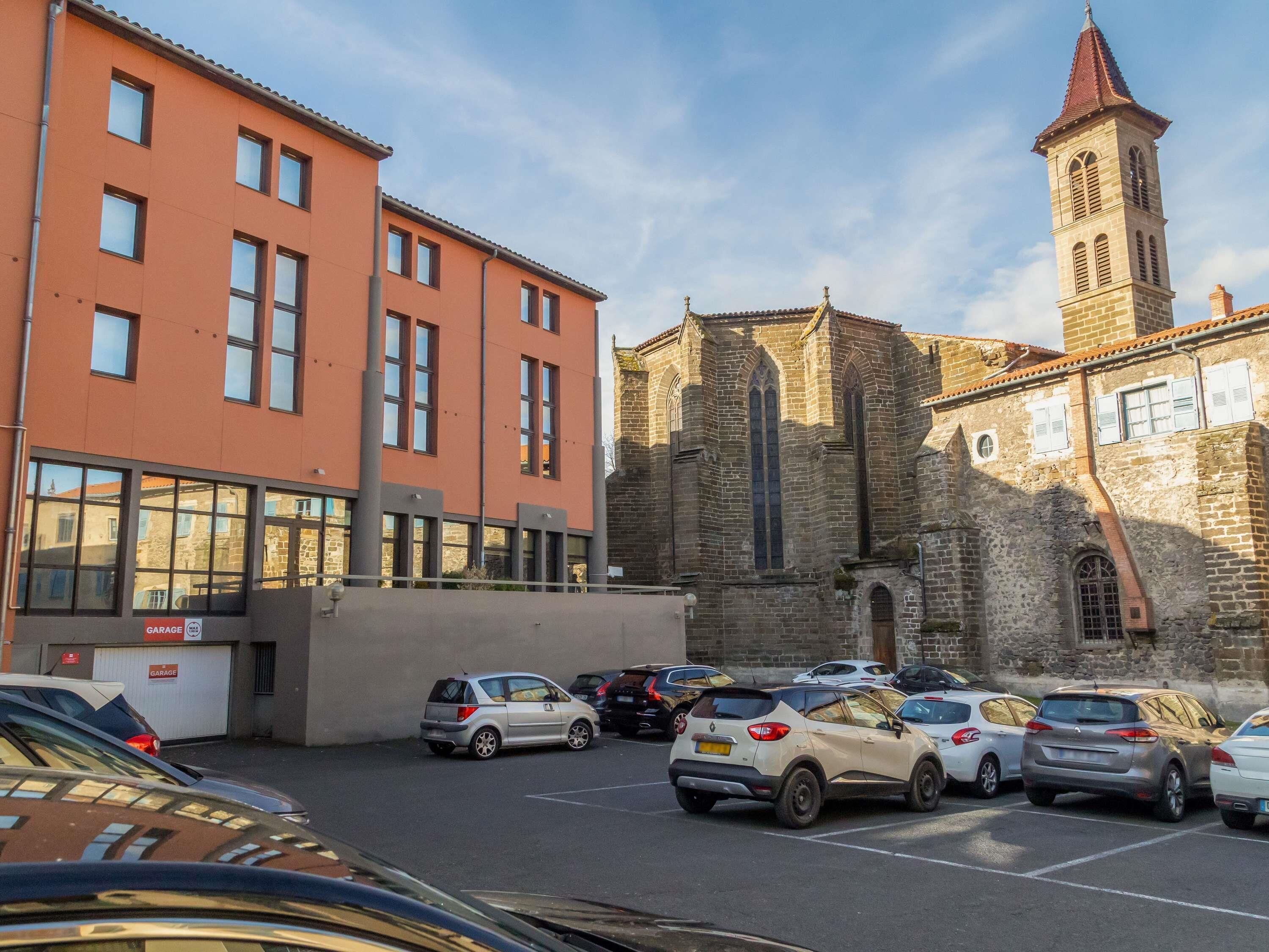 Un estacionamiento con varios autos, un edificio de fachada roja y una iglesia con un campanario.