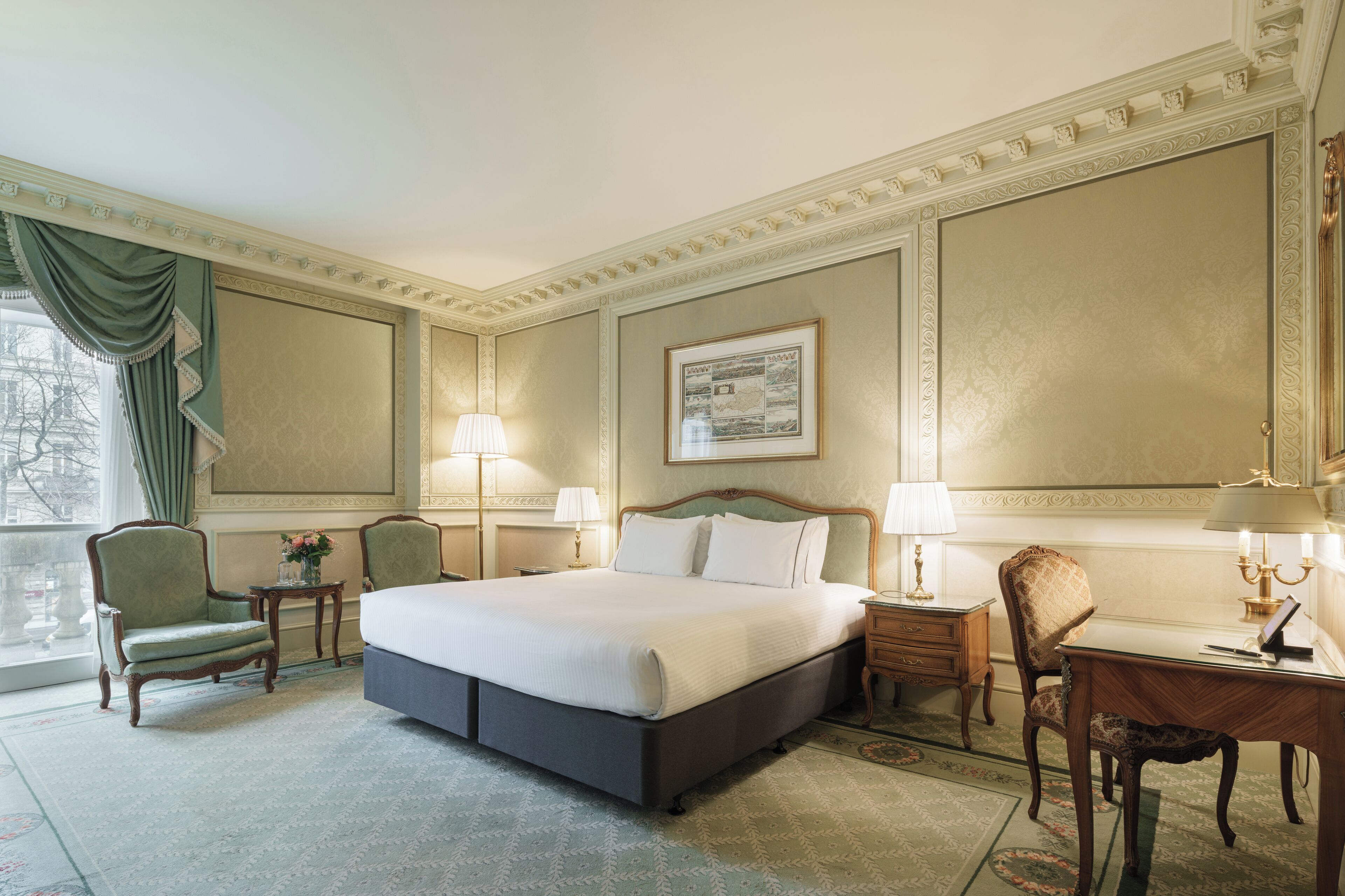 Una habitación de hotel con una cama grande, dos sillas, un escritorio y una lámpara.