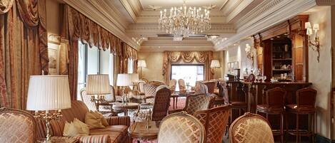 Un lobby de hotel lujoso con muebles ornamentados, una lámpara de araña imponente y una zona de bar.