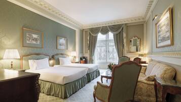 A hotel room with two beds, a sofa, a chair, a desk, and a window with curtains.
