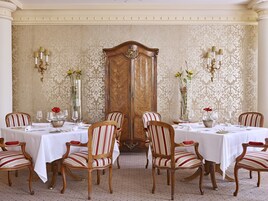 Uma sala de jantar formal com seis mesas, cada uma com toalhas brancas, cadeiras listradas e altos vasos com flores.