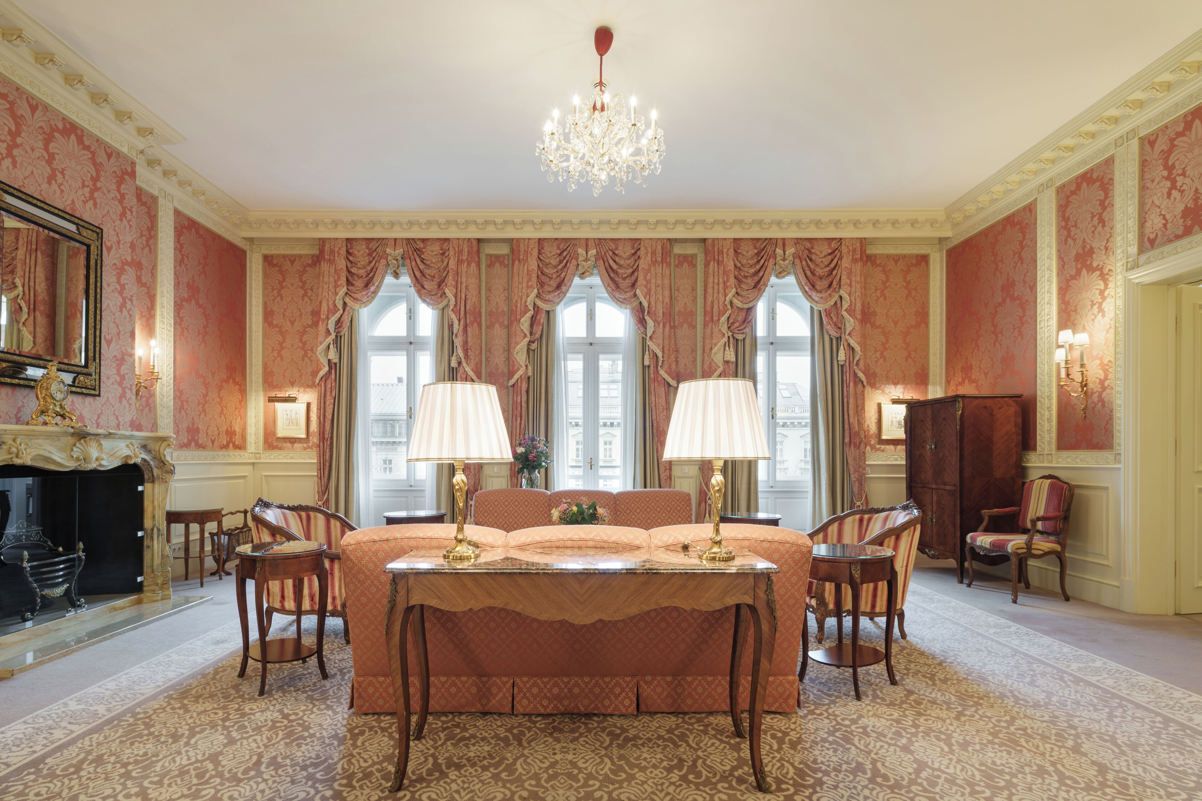 A luxurious bedroom with a large bed, two bedside tables, a chandelier, and a fireplace.
