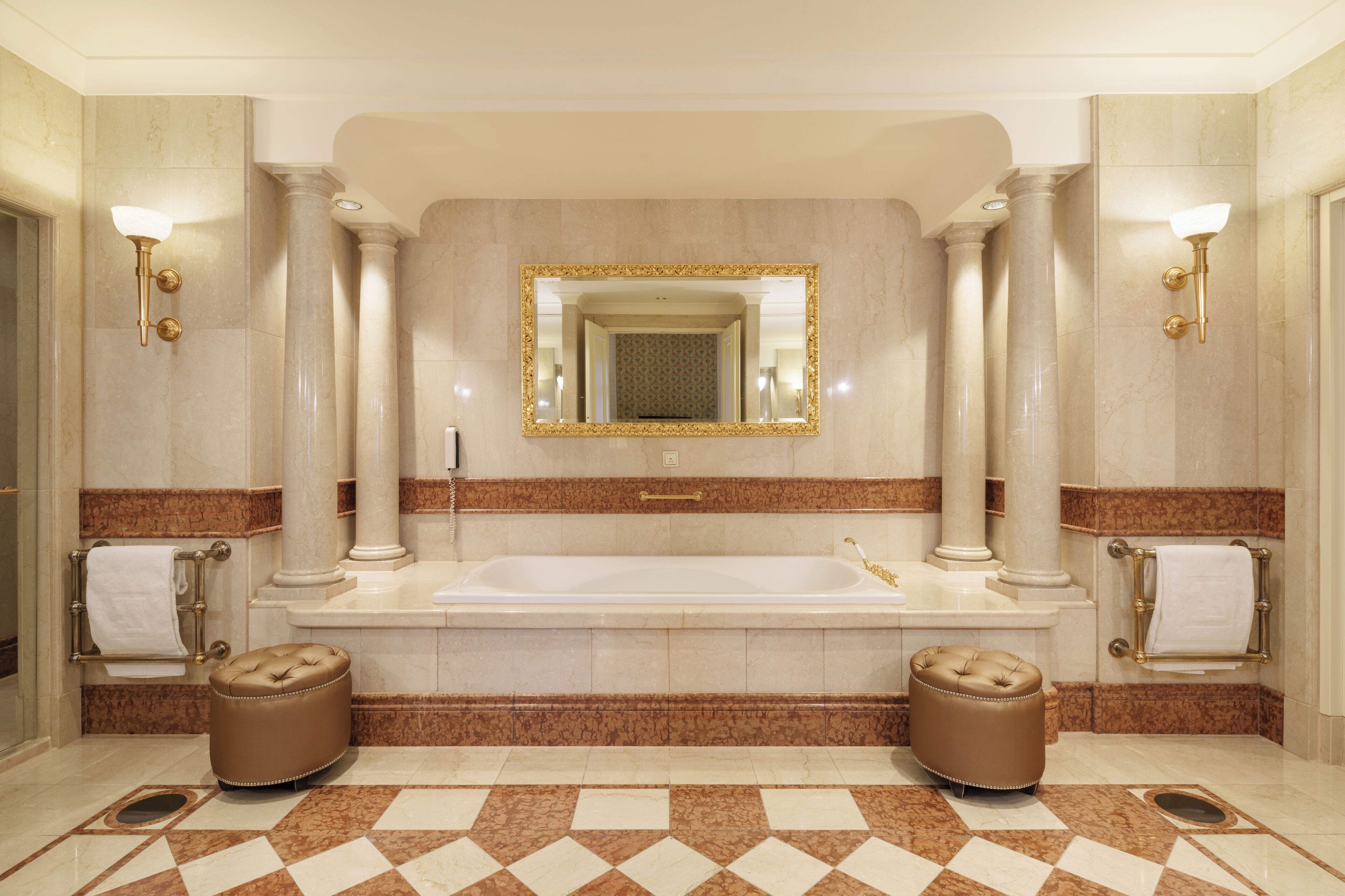 A luxurious bathroom with a large bathtub, two columns, a mirror, and marble flooring.