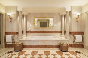 Une salle de bain luxueuse dotée d’une grande baignoire, de deux colonnes, d’un miroir et d’un sol en marbre.