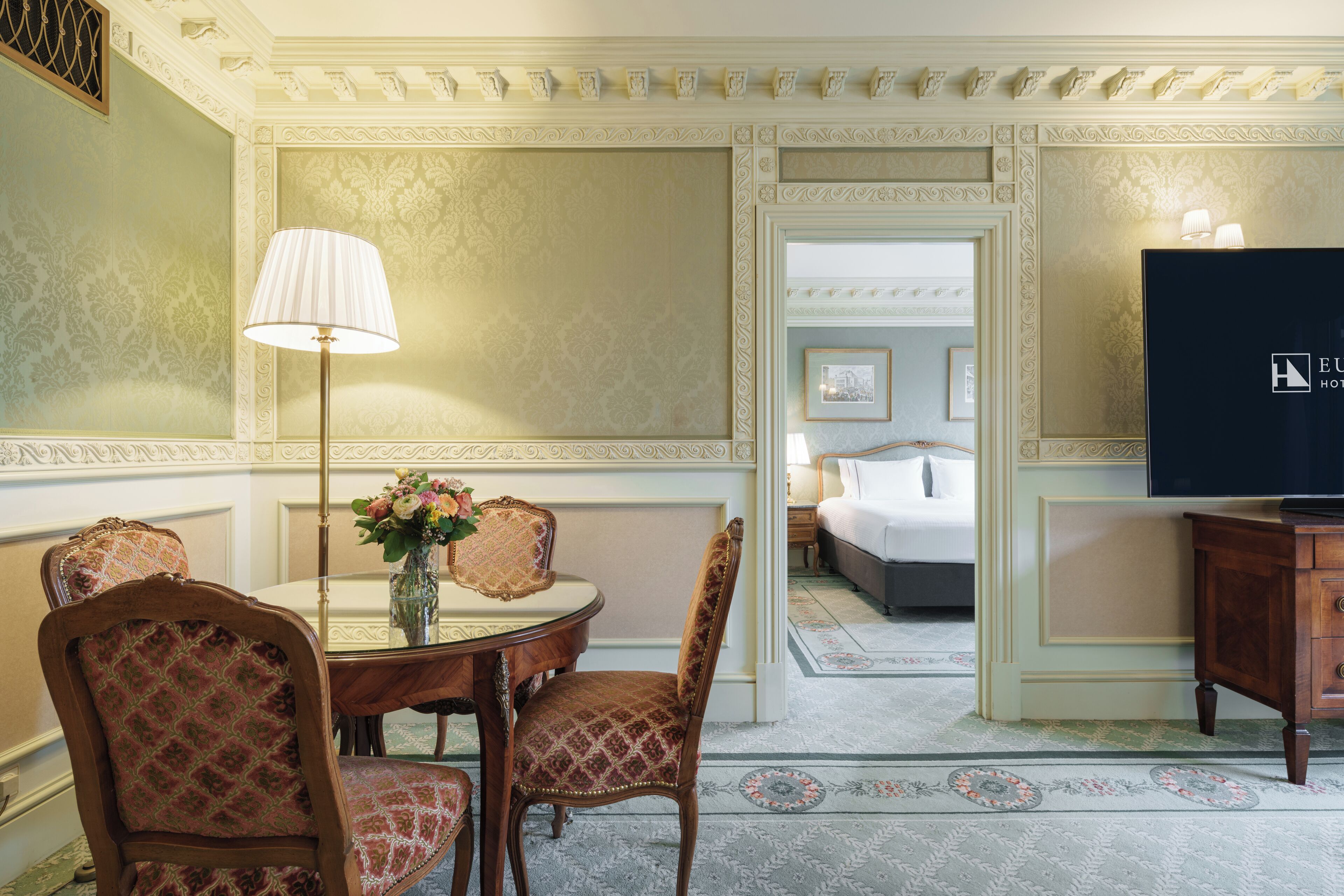 A hotel room with a dining area, a bed, and a TV.