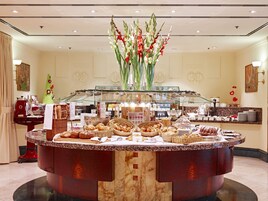 A buffet with various breads and pastries, a glass display case, and a vase with flowers.