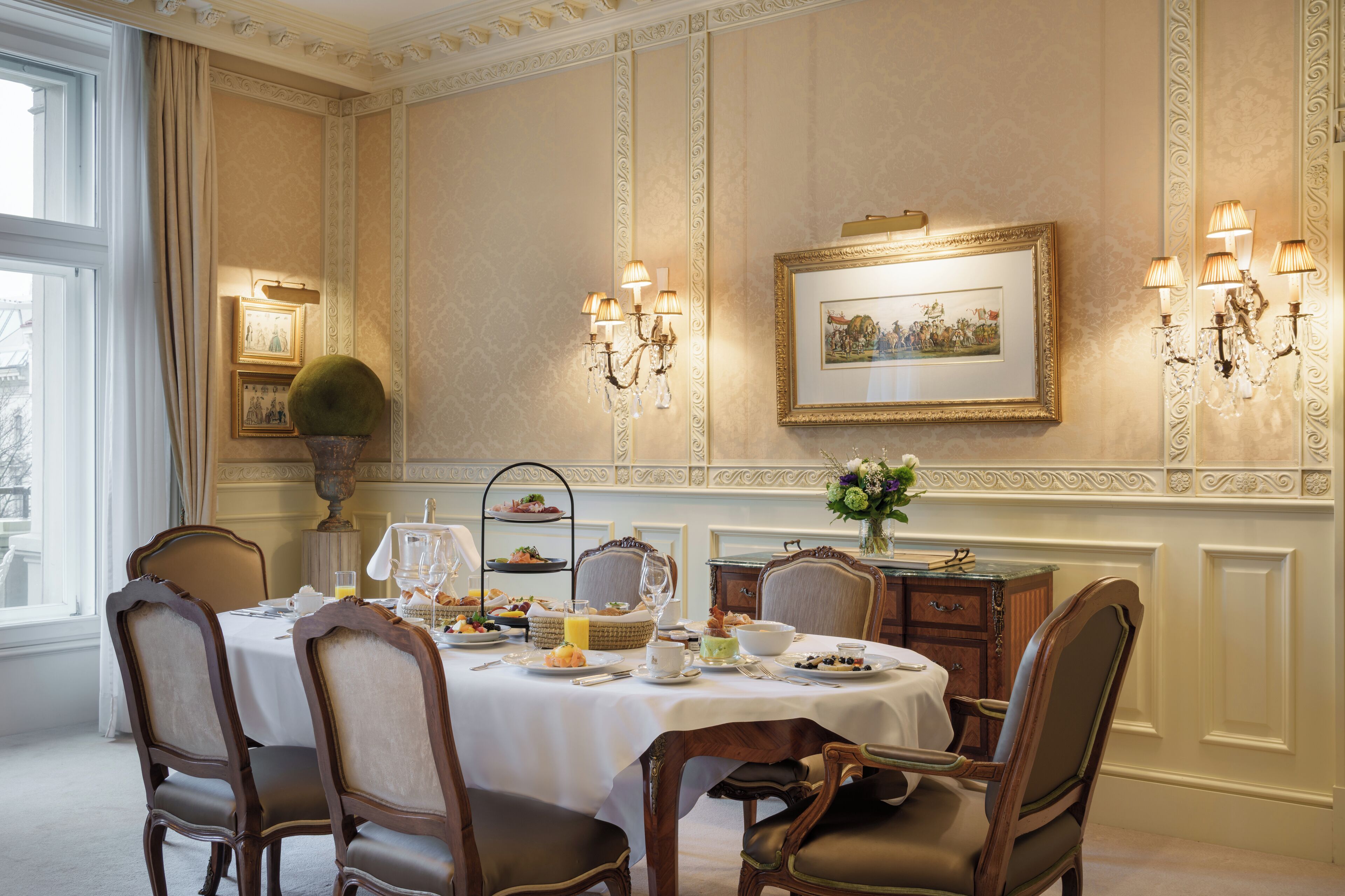A formal dining room with a table set for four, elegant chairs, a chandelier, and framed artwork on the wall.