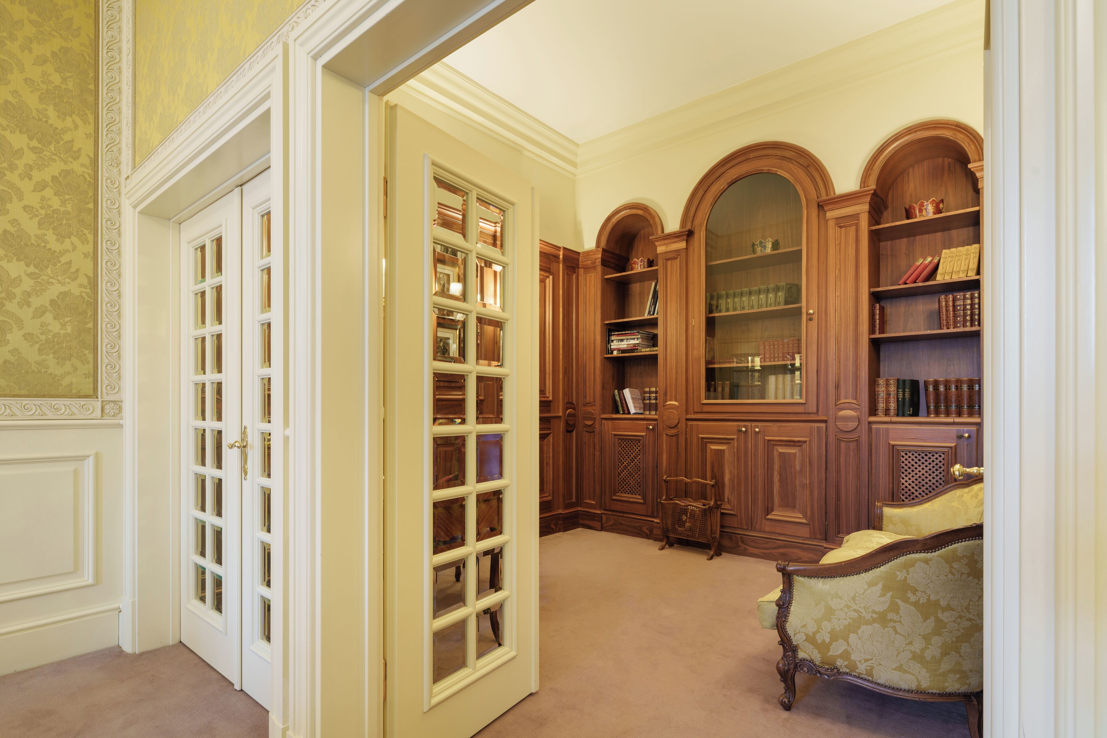 A library with wooden bookshelves, a reading chair, and a door with glass panels.