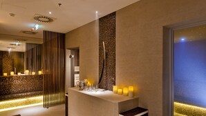 Une salle de bain moderne avec un grand miroir, un lavabo décoré de bougies et un mur à texture.