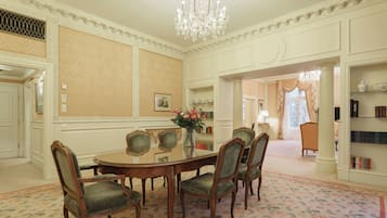A formal dining room with a glass table surrounded by upholstered chairs, a chandelier, and a patterned carpet.