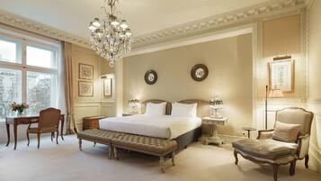 A spacious bedroom with a large bed, a sitting bench, a chair, a desk, and a chandelier.