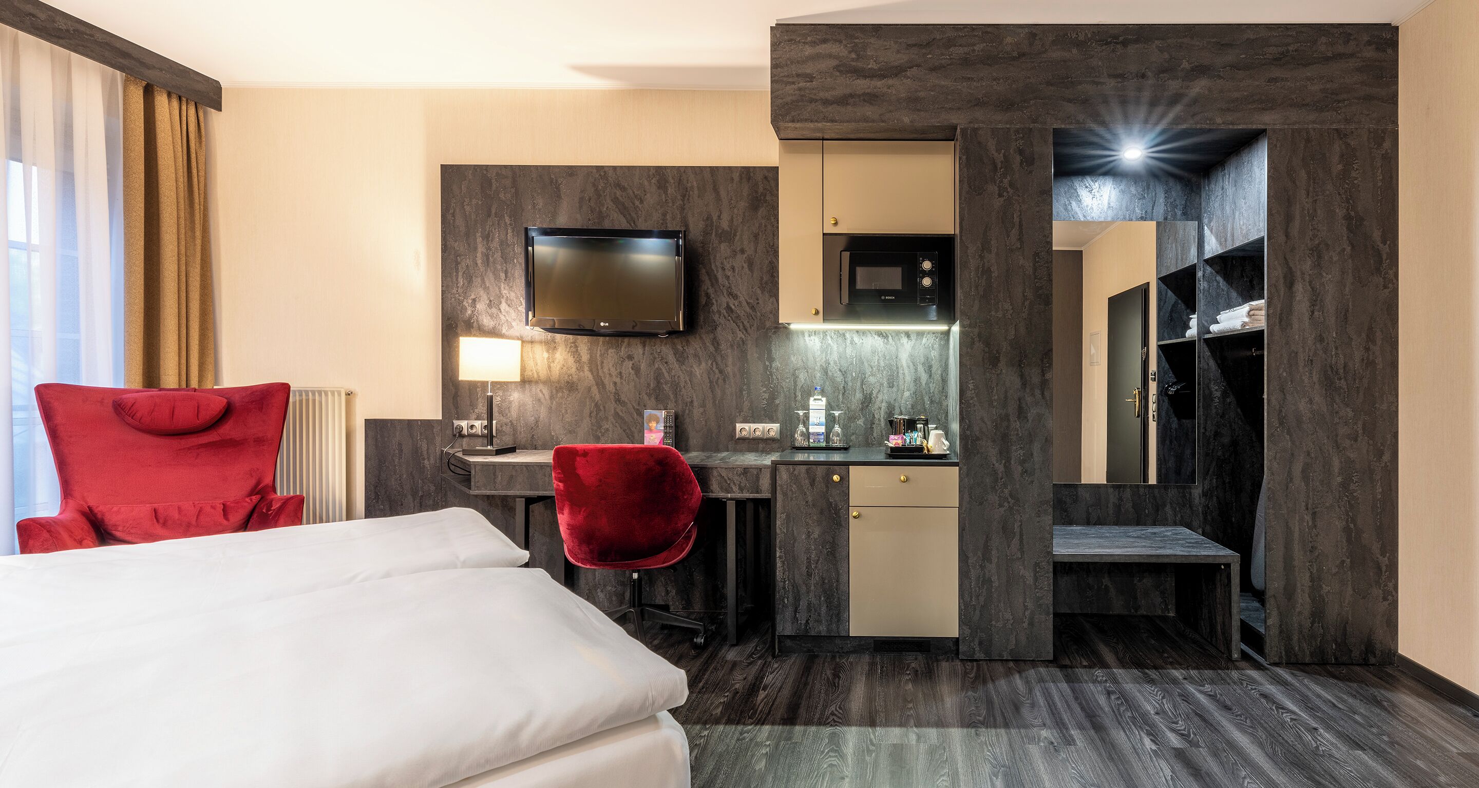 Hotellihuone, jossa on sänky, työpöytä, televisio, mikroaaltouuni ja vaatekaappi.