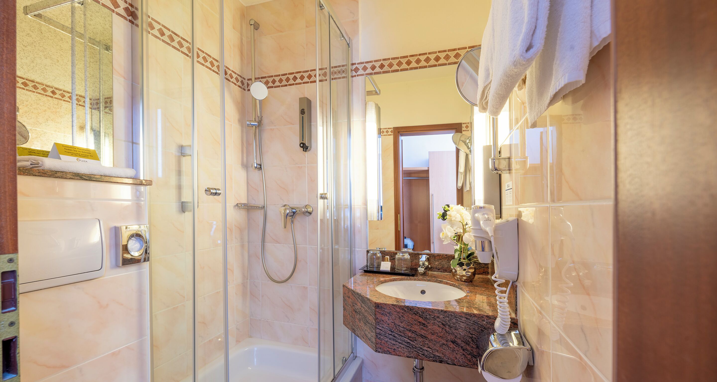 A bathroom with a glass-enclosed shower, a sink with a marble countertop, and a mirror.