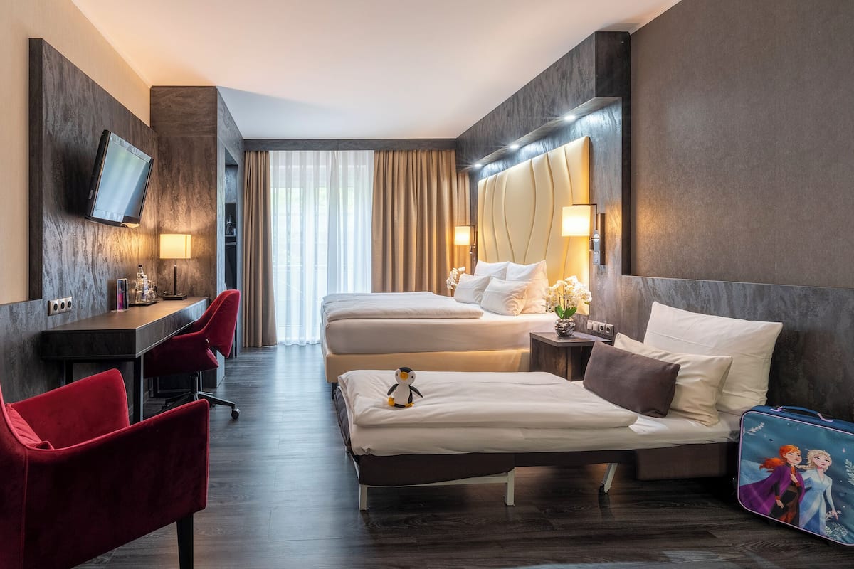 Quarto de hotel com cama, escrivaninha, cadeira, televisão e mala.
