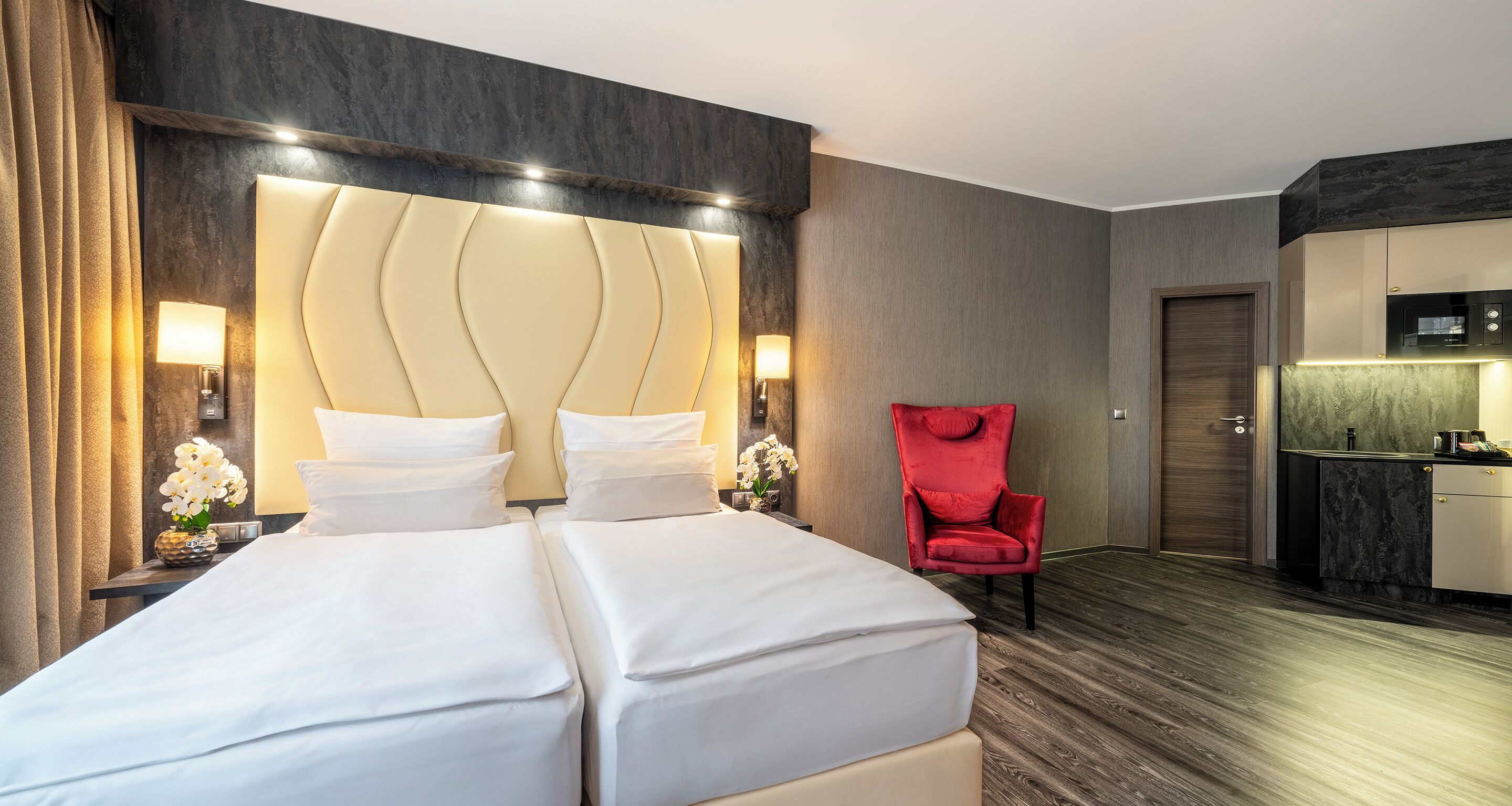 Una habitación de hotel con una cama grande, un sillón rojo, un escritorio pequeño y una kitchenette.