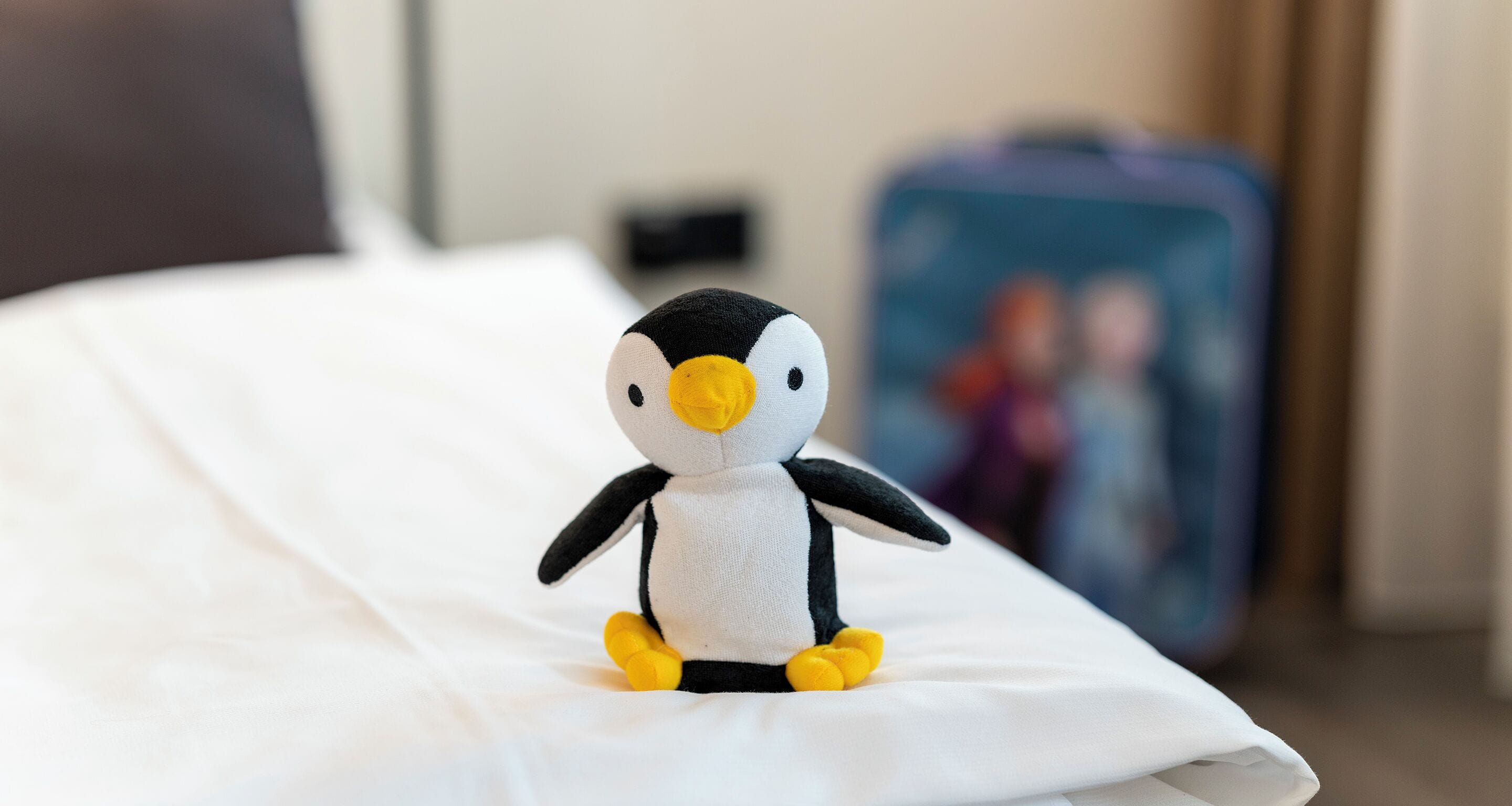 A plush penguin toy on a bed with a blurred background.