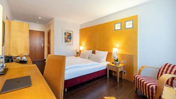 Ein Hotelzimmer mit einem Bett, einem Schreibtisch mit Laptop, einem Stuhl und einem Nachttisch mit Lampe.