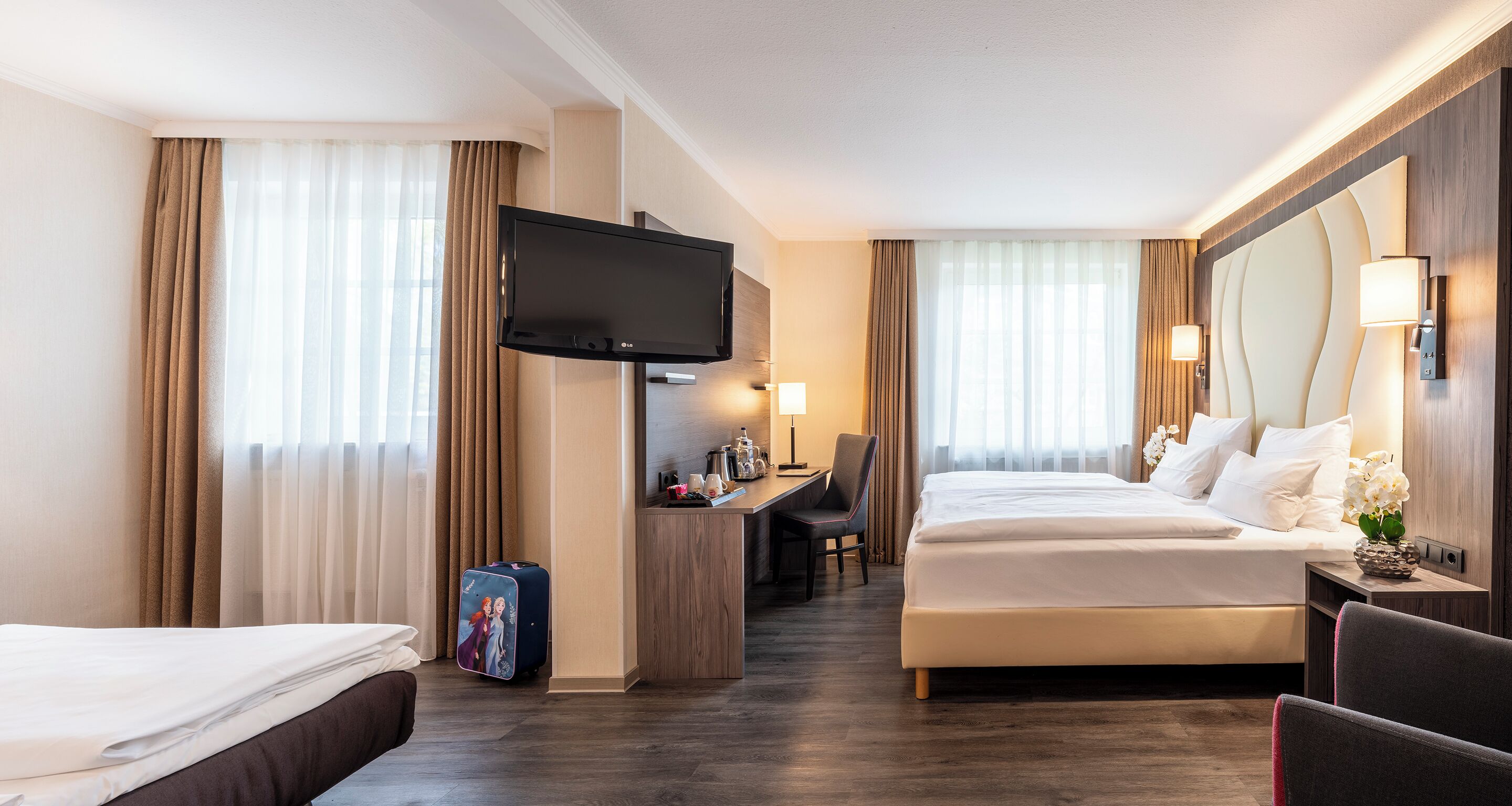 Una habitación de hotel con una cama, un escritorio, una silla, un televisor y una mesita de noche con lámpara.