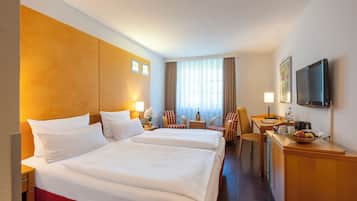 A hotel room with two beds, a desk with a chair, a TV, and a window with curtains.