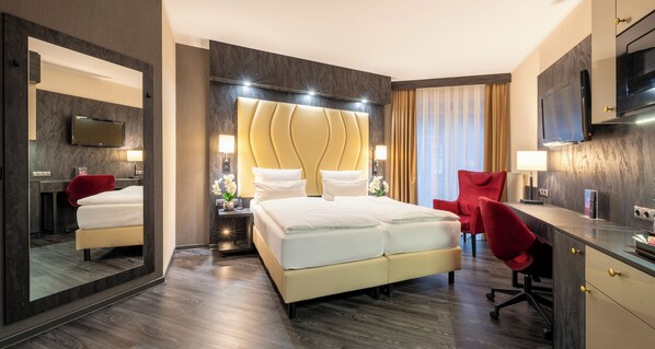 Une chambre d’hôtel moderne avec un grand lit, un bureau, une chaise rouge et un téléviseur.