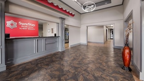A hotel reception area with a red sign for SureStay Plus by Best Western, a modern chandelier, and a large vase with dried flowers. - SureStay Plus Hotel by Best Western San Antonio North (San Antonio)