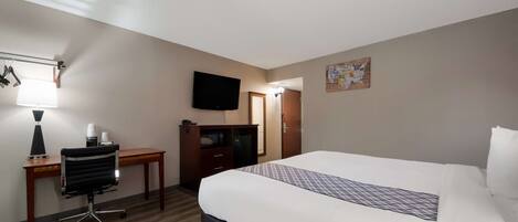 Una habitación de hotel con cama, escritorio, silla, televisor y una pequeña mesa con lámpara.
