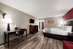 Una habitación de hotel con cama, escritorio, silla y televisor en la pared.