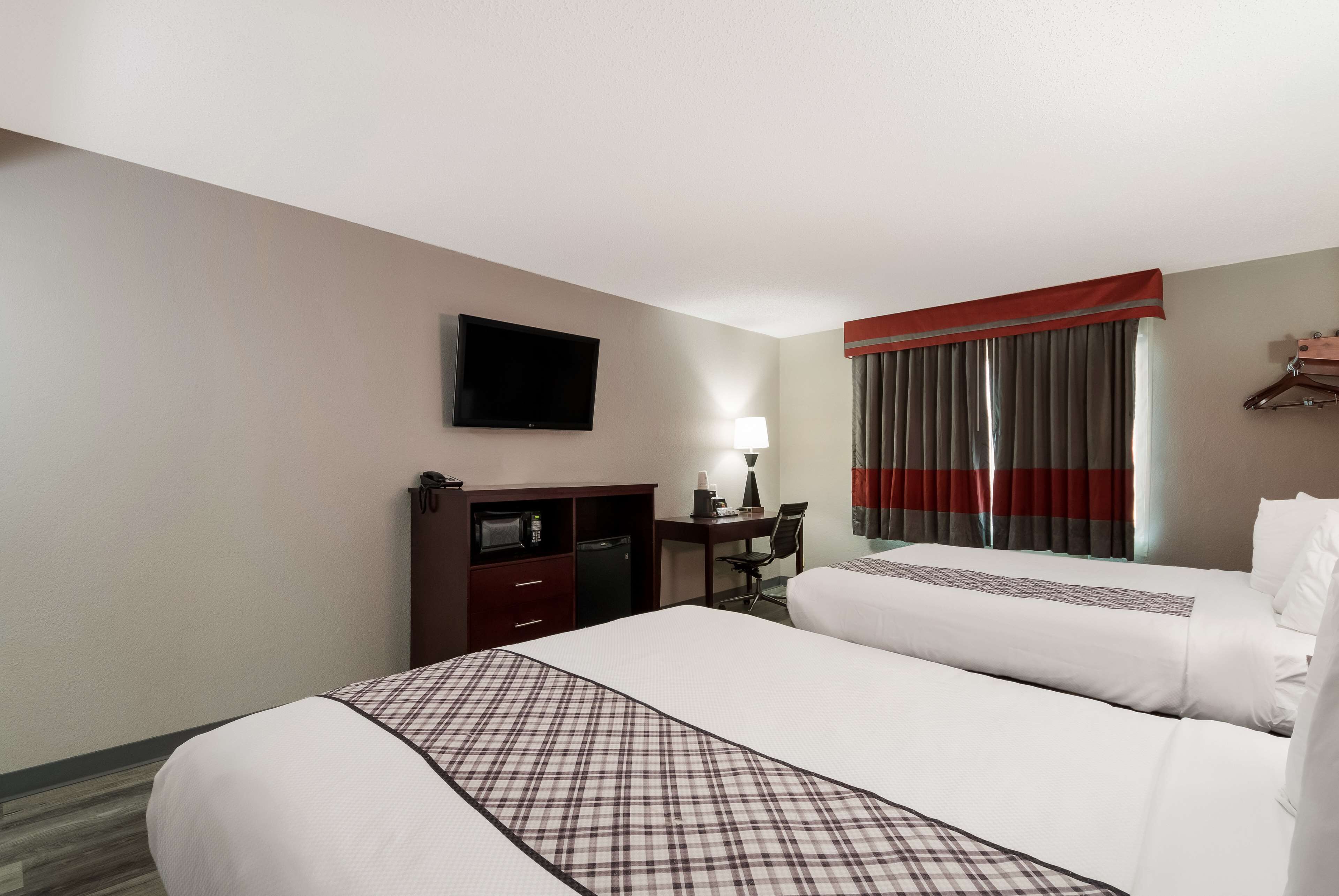 A hotel room with two beds, a TV, a desk with a lamp, and a wardrobe.