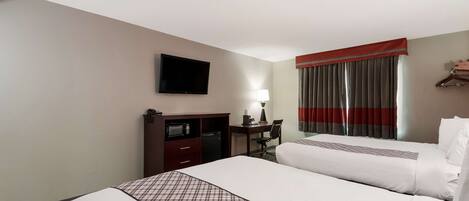 A hotel room with two beds, a TV, a desk with a lamp, and a wardrobe.