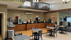 A hotel lobby with a wooden reception desk, a clock, and a coffee machine. There are tables and chairs arranged for guests. - Quality Inn & Suites Grants - I-40 (Grants)