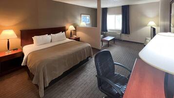 A hotel room with a bed, two bedside tables with lamps, a chair, a small table, and a window with curtains.