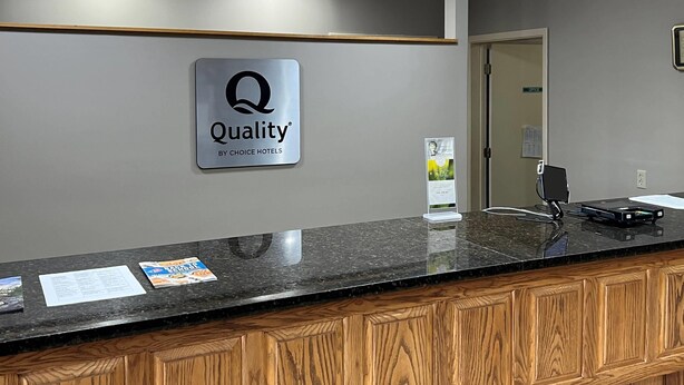A hotel reception area with a sign reading "Quality by Choice Hotels," a marble counter, and a wooden cabinet. - Quality Inn & Suites Grants - I-40 (Grants)