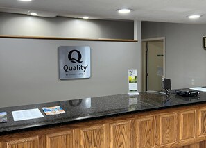 Hotellin vastaanottoalue, jossa on kyltti, jossa lukee ”Quality by Choice Hotels”, marmorinen vastaanottotiski ja puinen kaappi.