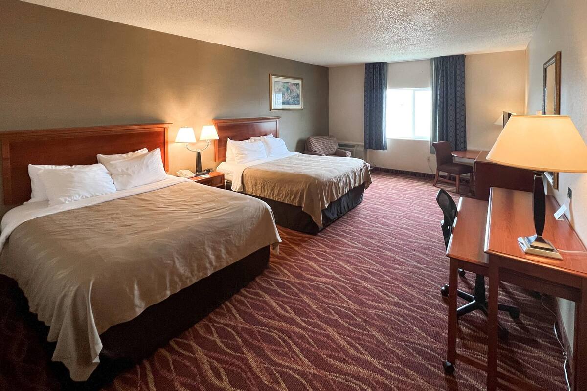 A hotel room with two beds, a desk, a chair, and a window with curtains.