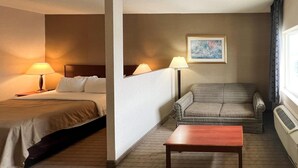 A hotel room with a bed, a sofa, a table, and a painting on the wall. - Quality Inn & Suites Grants - I-40 (Grants)