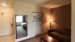 A hotel room with a wooden floor, a sofa, a table, a lamp, a mirror, and a door. - Quality Inn & Suites Grants - I-40 (Grants)