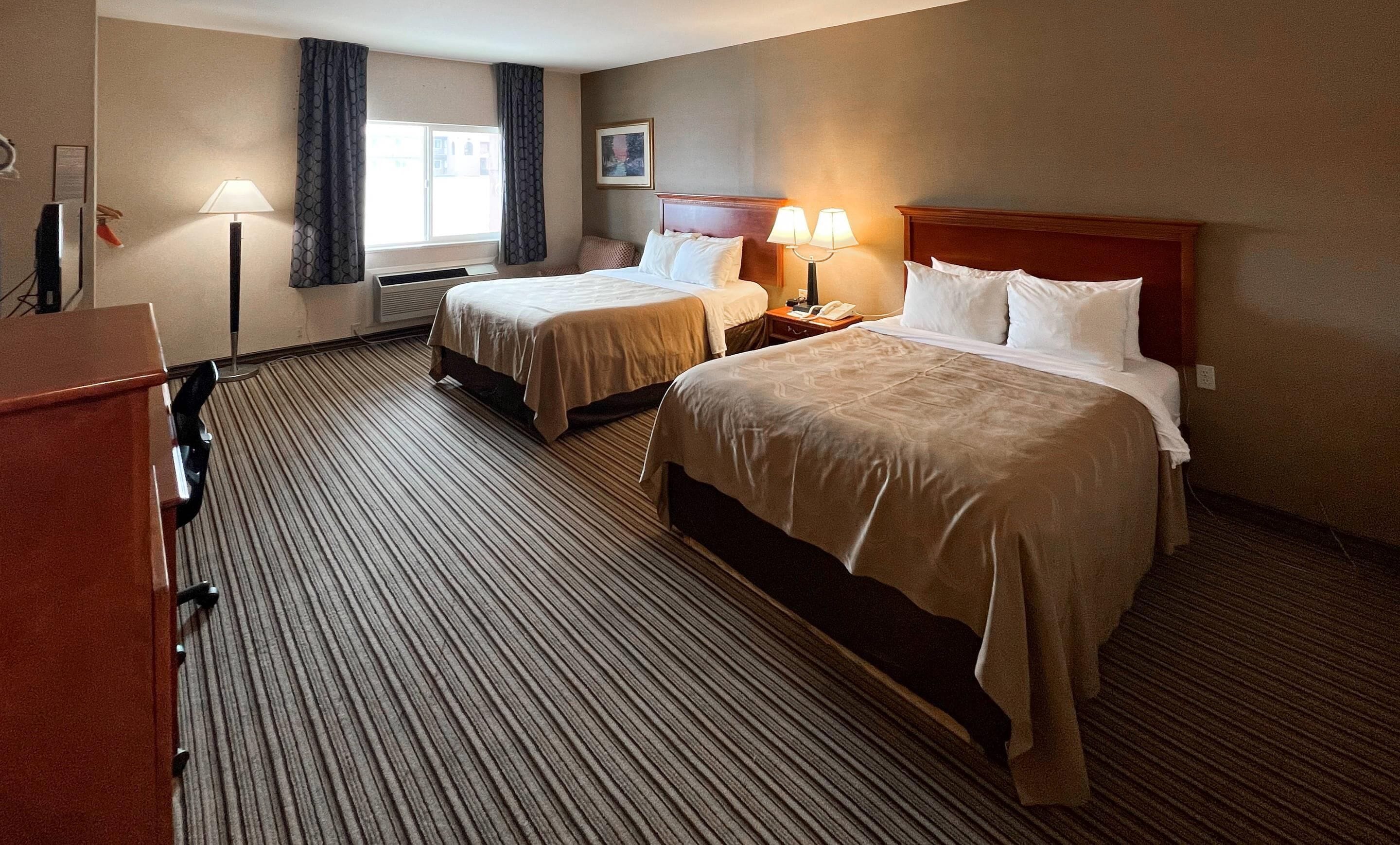 Habitación de hotel con dos camas, un escritorio, una lámpara y una ventana.